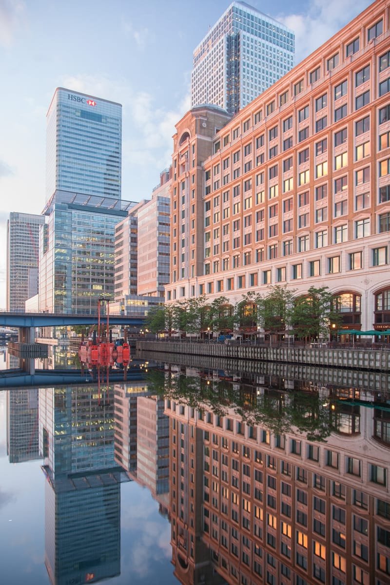 Brick warehouse and glass towers reflected in the dock at sunrise