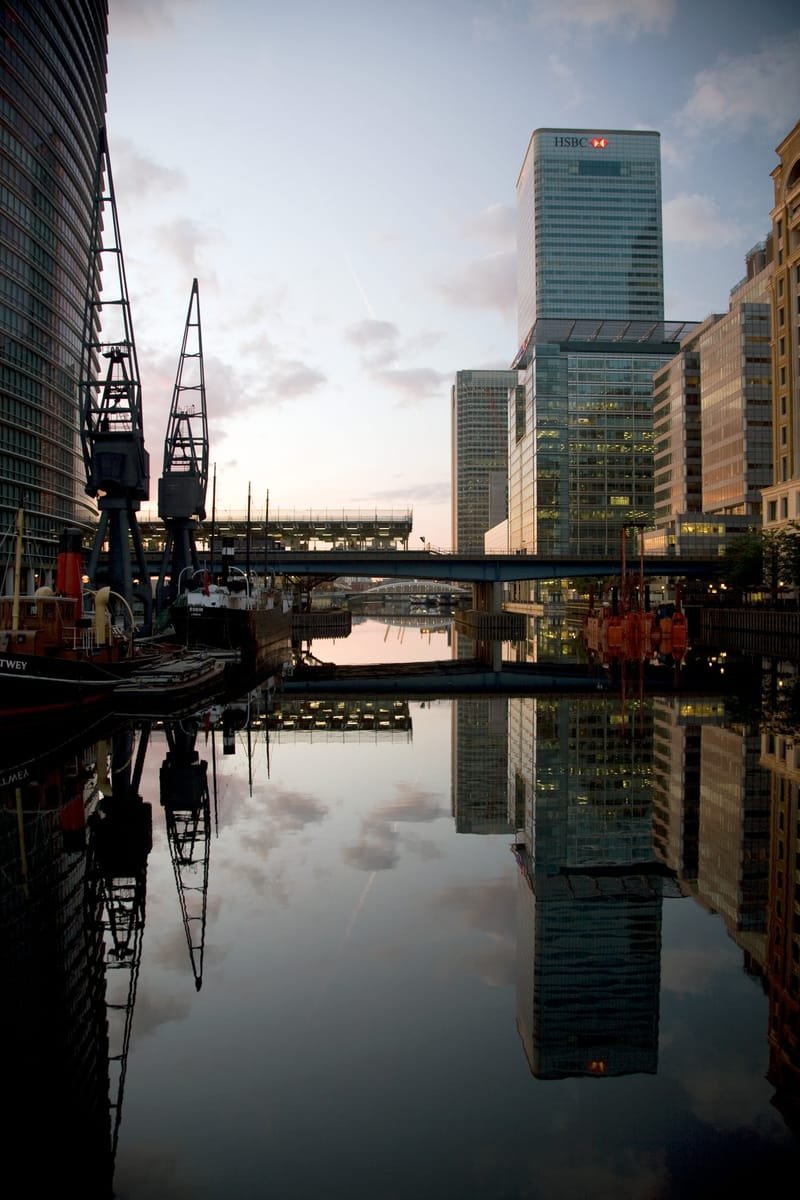 Dock cranes and Canary Wharf towers reflected in calm water at sunrise