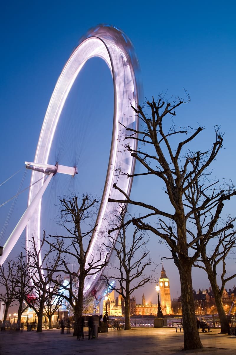 The London Eye turning at twilight, motion-blurred against a deep blue sky, Big Ben beyond