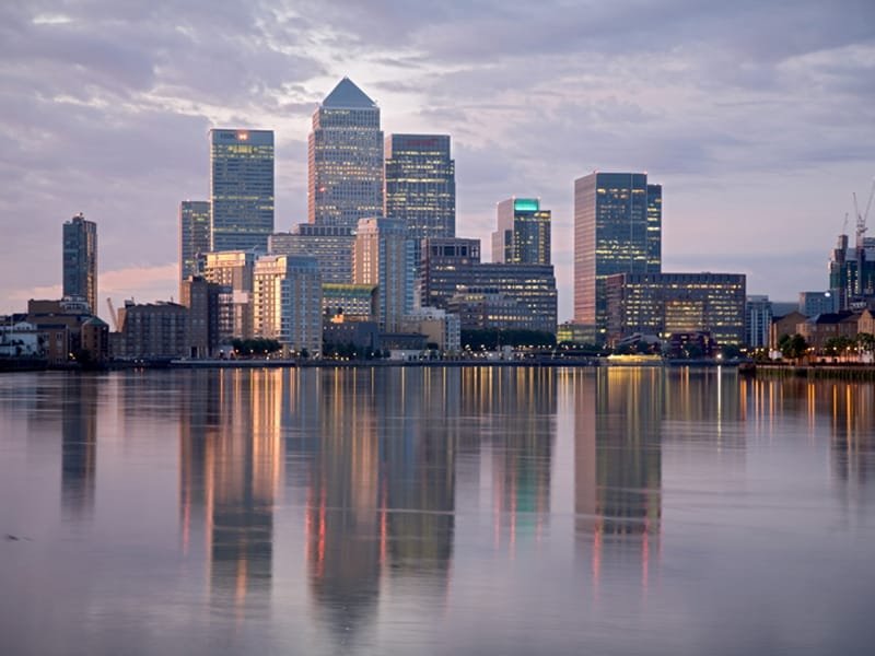 Canary Wharf towers at dawn across still water, lights still burning