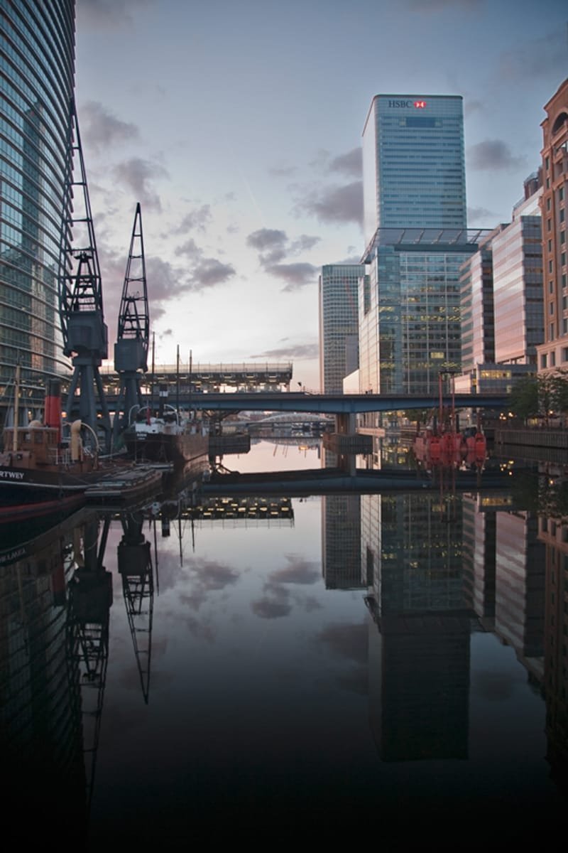 Dockside cranes and Canary Wharf towers mirrored in the dock at dawn