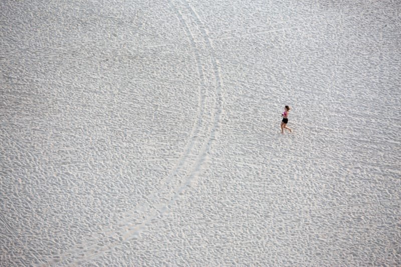 A lone runner crossing a vast expanse of pale sand, seen from above, UAE