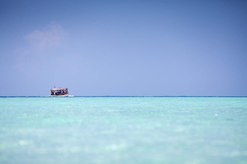 Small boat crossing a flat turquoise sea under a hazy sky, Maldives