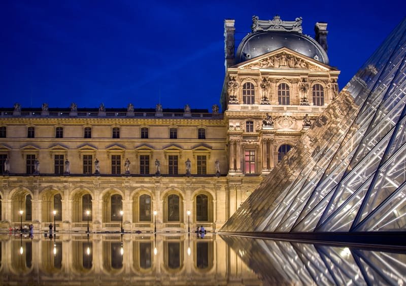 The Louvre and its glass pyramid floodlit at night, reflected in still water