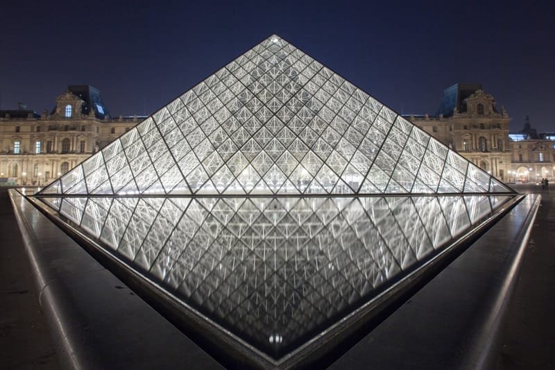 The Louvre pyramid glowing at night between the palace wings