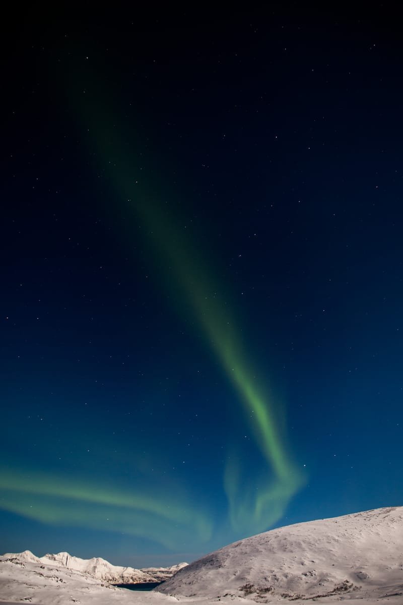 A green arc of the northern lights over a snow-covered ridge