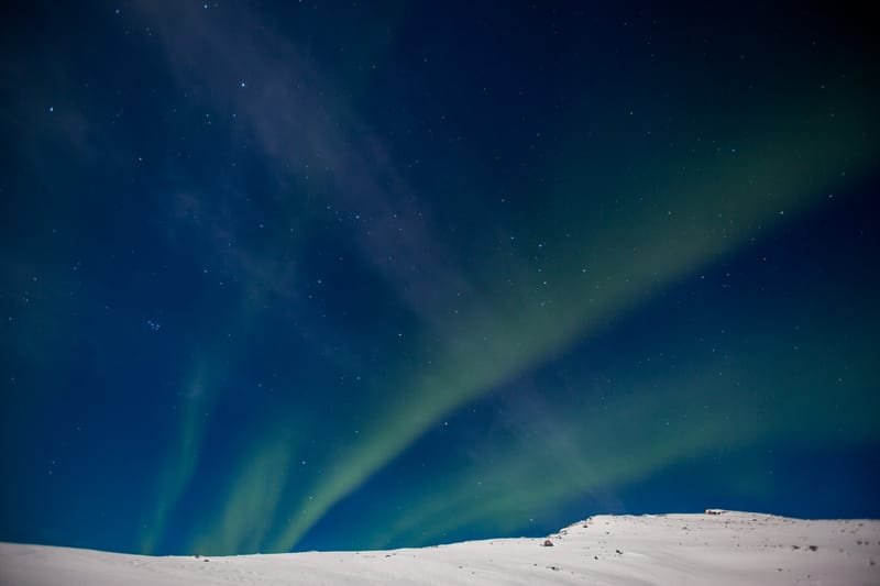 The northern lights rippling above snowy hills under a starry sky