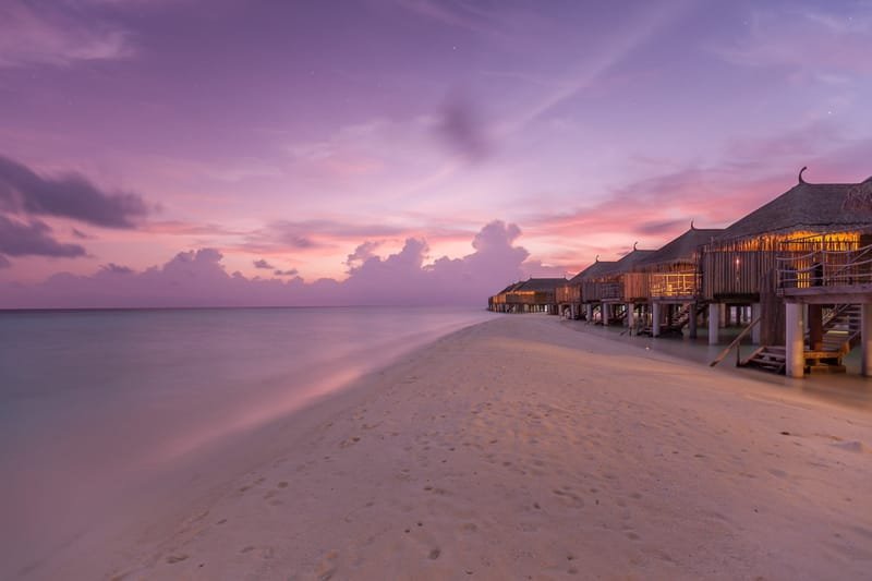 Overwater villas at the end of a sand spit under a violet dusk sky, Maldives