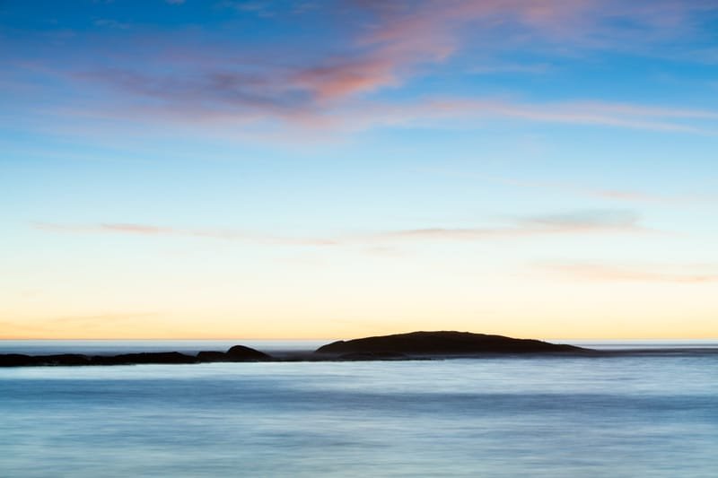 An island on the horizon under a pastel dusk, long-exposure water