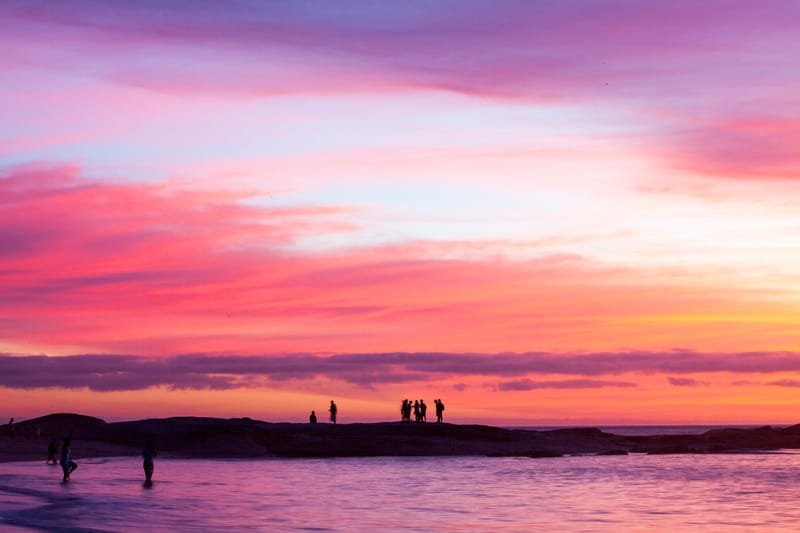 Bathers silhouetted on shoreline rocks under a vivid pink sunset, Rio de Janeiro