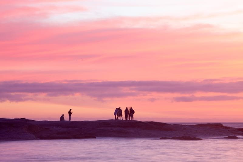 Figures on a rocky shore beneath a pink-striped sunset sky, Rio de Janeiro
